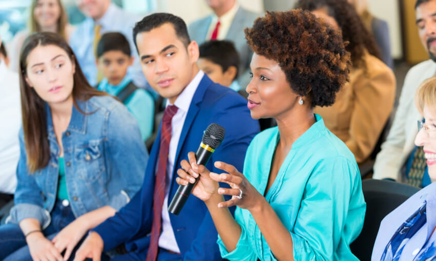 African American woman asks question during a town hall or seminar style meeting