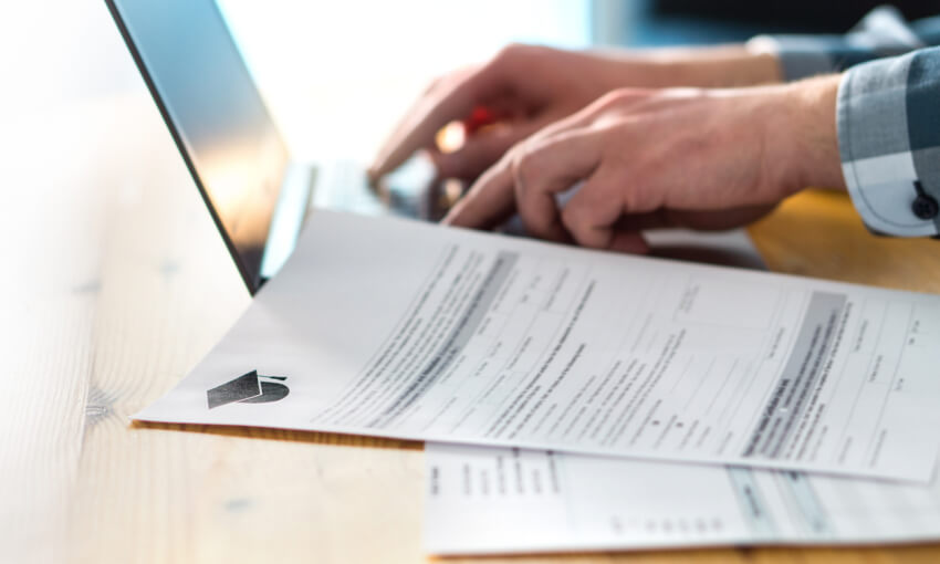 Young man writing college or university application form with laptop.