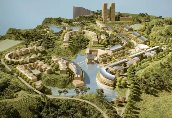 A digital rendering shows an aerial view of a model of the initial campus plans designed by Moshe Safdie for the Asian University for Women. The model has curving green spaces, roads, small bodies of water, and beige buildings.