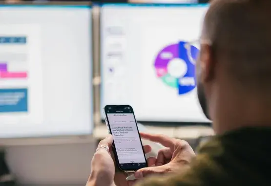 Data on screens in background with man using phone in the foreground. 