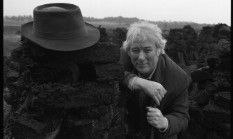 Seamus Heaney at a turf bog in Bellaghy with his father's coat, hat and walking stick and additional shots in the Bellaghy bog, 1986.  Bobbie Hanvey, photographer.