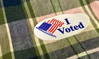 An "I Voted" sticker on plaid fabric.