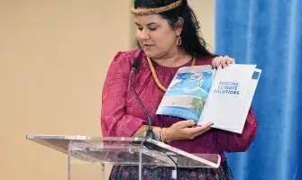 Commission member Leanne Kealoha Fox at podium with climate action report. 