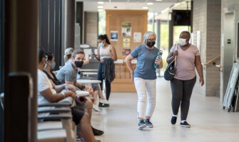 Two women walk through the annex of a community center gym and greet the people they see.