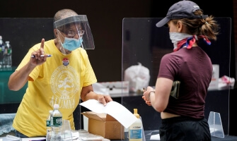 A poll worker and voter wear masks to prevent the spread of COVID-19 during a U.S. primary election.