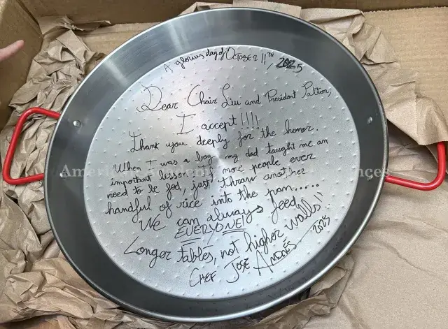 Color photograph of a silver paella pan with red handles, showing handwritten message in black ink