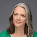A photo of Alison Darcy, a person with light skin and long gray-brown hair, wearing a green top and facing the viewer.