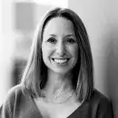 A black and white photo of Holly Dubois, a person with light skin and long dark hair, wearing a dark top and smiling at the viewer.