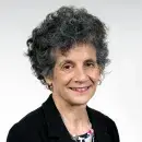 A photo of Sherry Glied, a person with light skin and dark curly hair, wearing a black suit and smiling at the viewer.