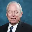 A photo of Alan Leshner, a person with light skin and short gray hair, wearing a dark suit and white shirt, and smiling at the viewer.
