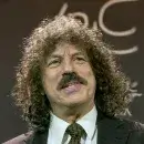 A photo of Robert Levenson, a person with light skin, long brown curly hair, and a brown mustache, wearing a dark suit and white shirt, and facing the viewer.