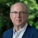A photo of Peter Slavin, a person with light skin and short gray hear, wearing glasses, a dark suit, and white shirt, and facing the viewer .