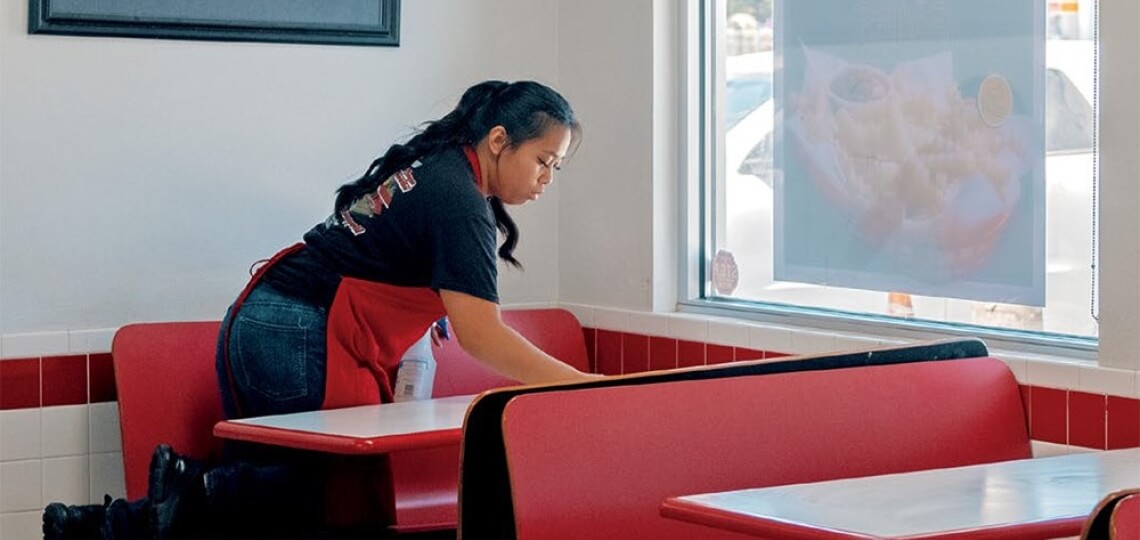 Woman in a Red Apron Wiping Down a Restaurant Table