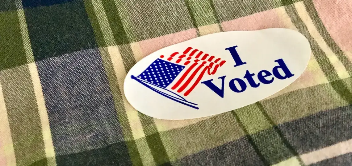 An "I Voted" sticker on plaid fabric. 