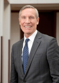 A headshot of David W. Oxtoby, a man with short gray hair. Oxtoby wears a white dress shirt with a navy blue tie and gray suit. Photo by Martha Stewart Photography.