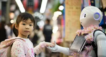 A young girl is looks at the viewer while her hand is held by a robot.