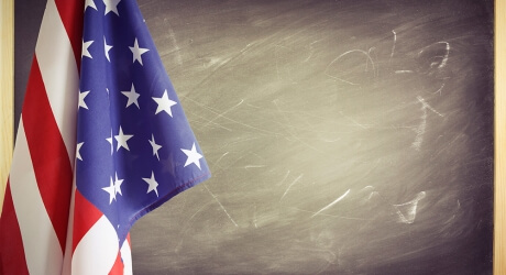 Photo of the American flag hanging over the left of a blank chalkboard