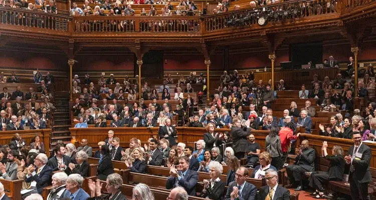 A multi-tiered, wooden auditorium filled with a formally dressed audience.