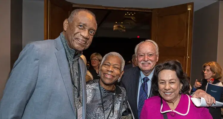 Four formally dressed adults pose and smile at a reception.