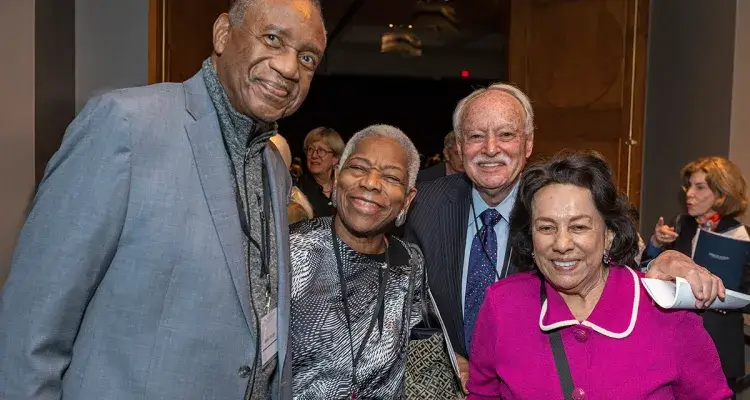 Four formally dressed adults pose and smile at a reception.
