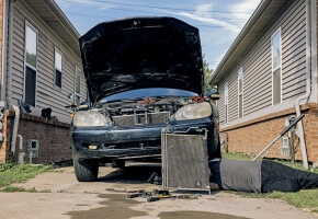 A person working under a car in a driveway. Their face is not visible. 