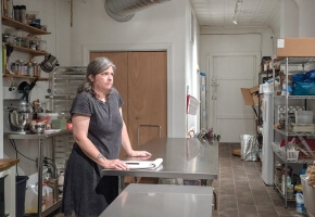 A person with pale skin with their hands on a steel table in the backroom of a tea shop. Their face indicates concern. 