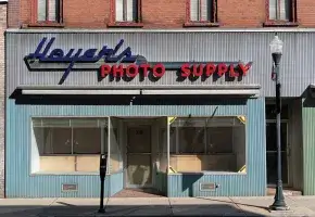 A vacant storefront with empty windows. Stickers in its right window announce Nikon cameras were once sold inside.