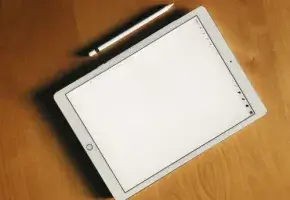 Tablet with blank screen with stylus on a woodgrain surface.
