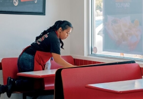 Woman in a Red Apron Wiping Down a Restaurant Table