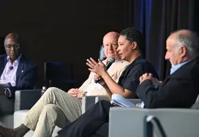 Four adults sitting on stage for a panel; one panelist is holding a microphone. 
