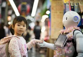A young girl is looks at the viewer while her hand is held by a robot.