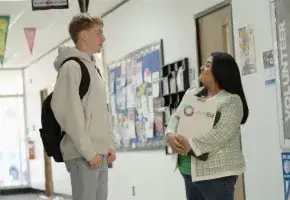 Hallway conversation in a school with a student and advisor from rootEd Alliance. 