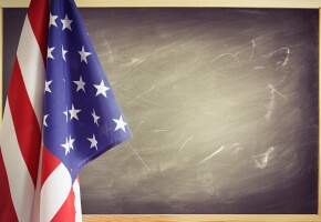 Photo of the American flag hanging over the left of a blank chalkboard