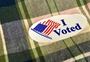 An "I Voted" sticker on plaid fabric. 