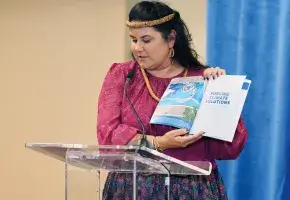 Commission member Leanne Kealoha Fox at podium with climate action report. 