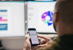 Data on screens in background with man using phone in the foreground. 
