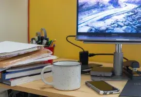 Desktop with computer, phone, mug, and a stack of books. 