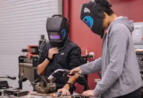 Two students in a shop class using equipment. 