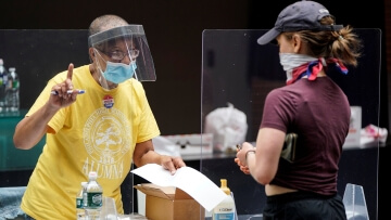 A poll worker and voter wear masks to prevent the spread of COVID-19 during a U.S. primary election.