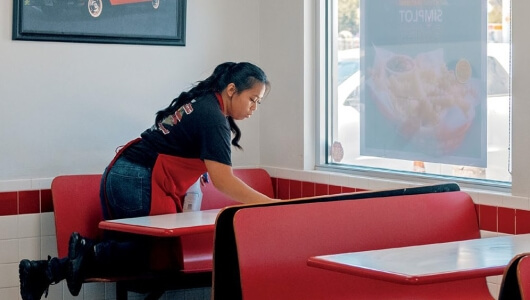 Woman in a Red Apron Wiping Down a Restaurant Table