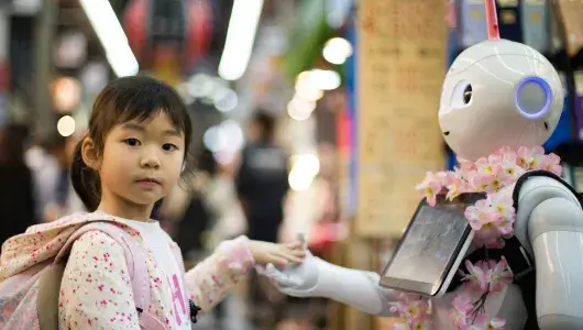 A young girl is looks at the viewer while her hand is held by a robot.