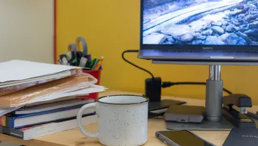 Desktop with computer, phone, mug, and a stack of books. 