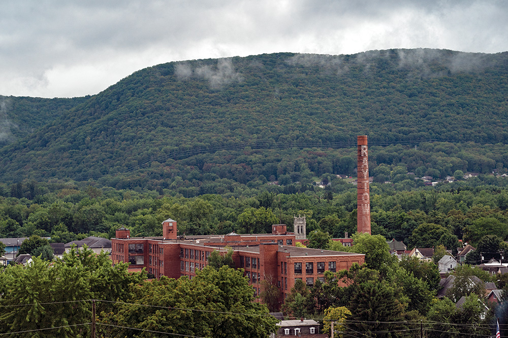 A factory building and some houses in a valley, with a single mountainside covered in trees.