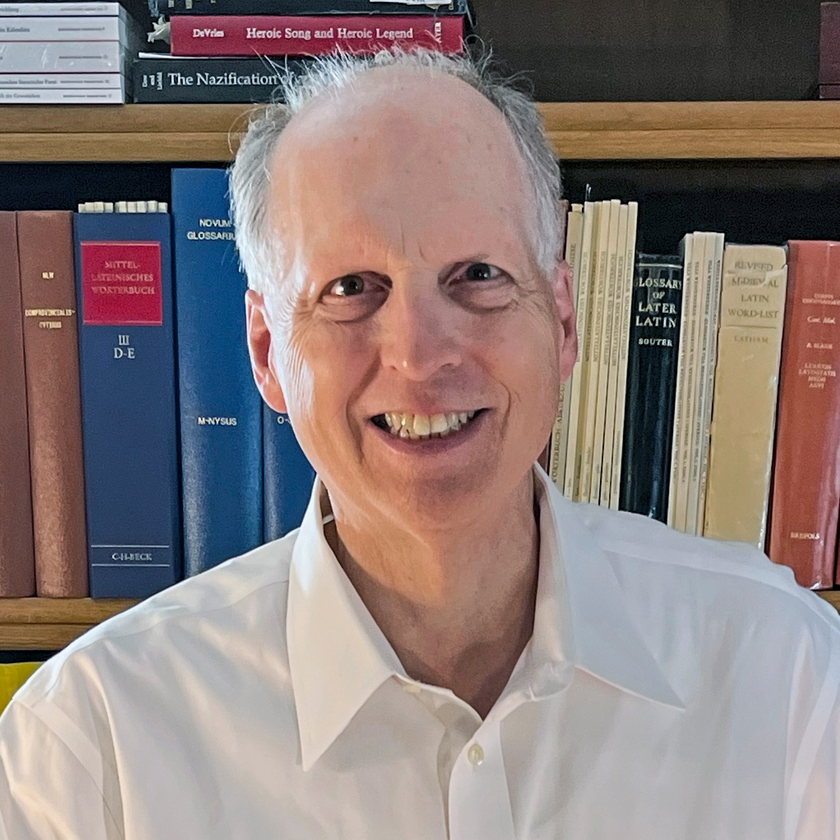 A person wearing a white button-up shirt is sitting in front of a bookshelf filled with books.